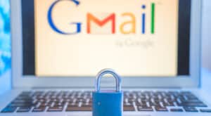 Blue closed metal lock on laptop touchpad with Gmail logo on the laptot screen in the background. Gmail security issues concept.