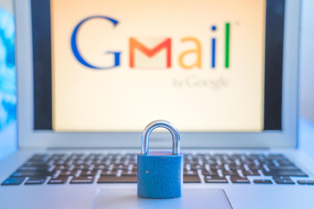 Blue closed metal lock on laptop touchpad with Gmail logo on the laptot screen in the background. Gmail security issues concept.